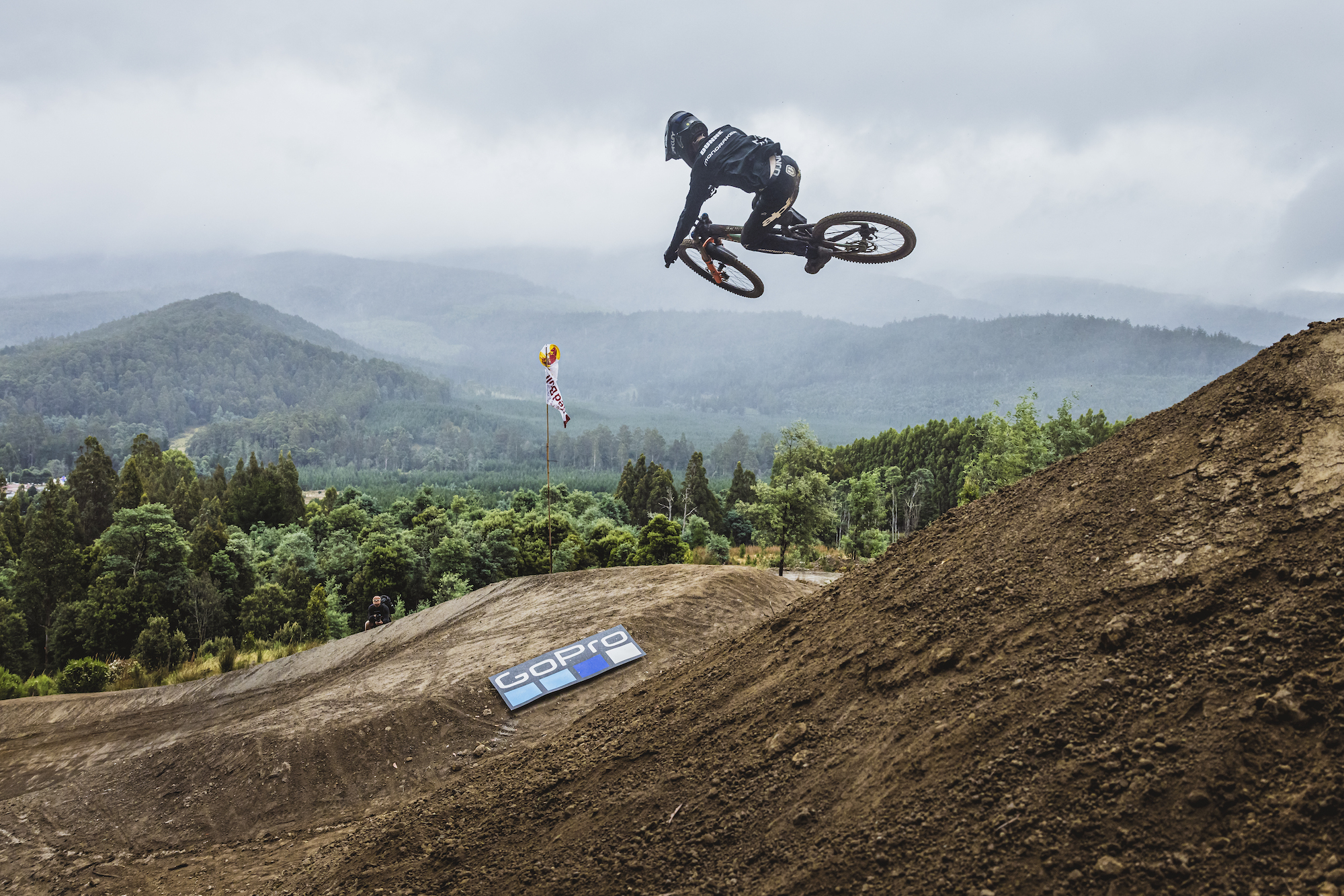 Rider mid-flight over the final gap jump with mountains behind